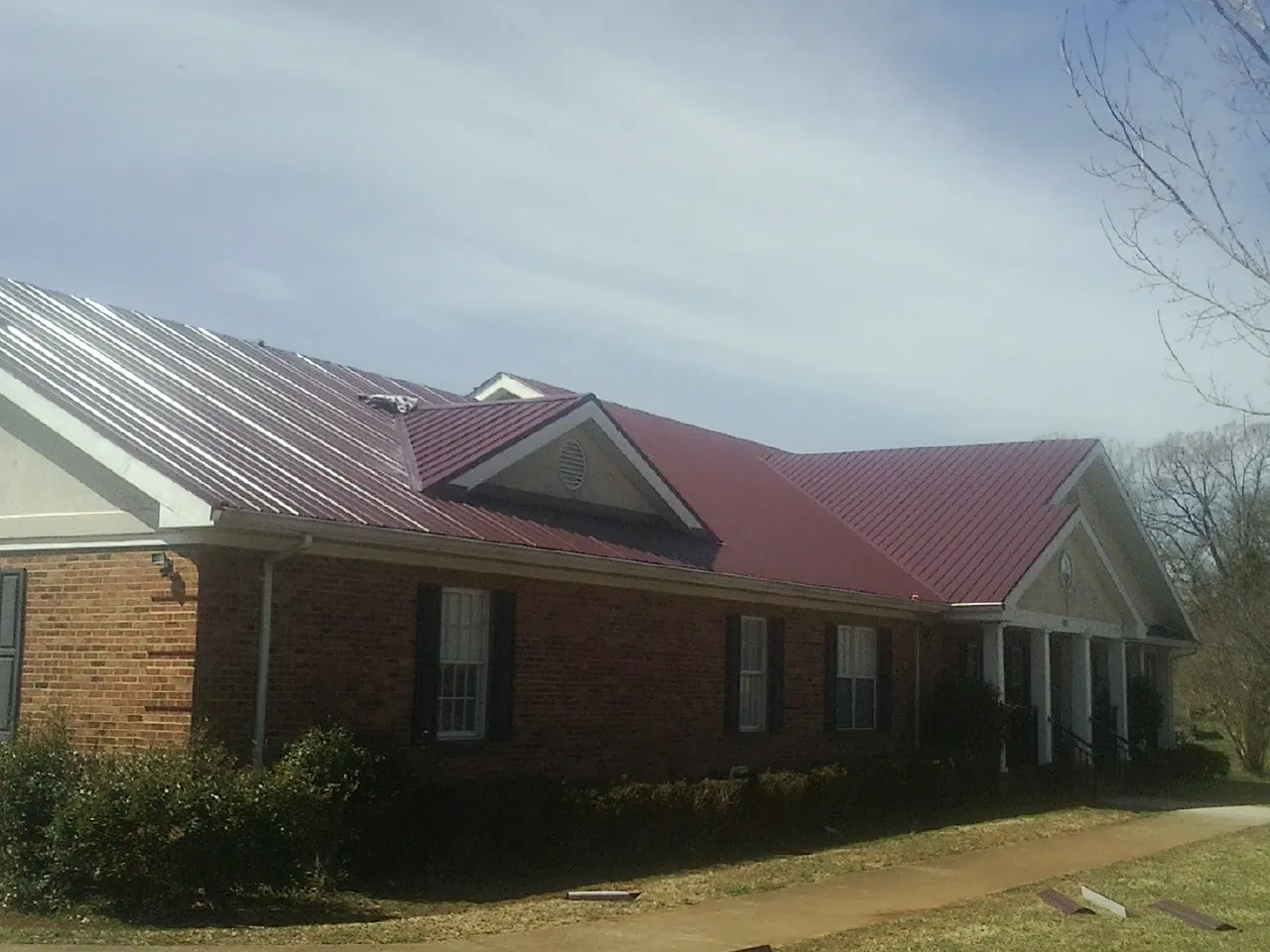 Red metal roof with gabled entries on a long brick building, from a Hail Damage Roof Repair job in Denver